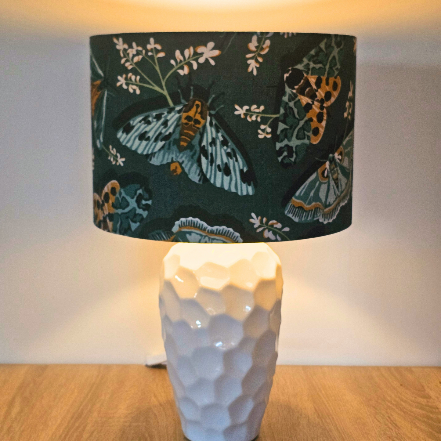Lamp with a decorative green lampshade featuring moth illustrations showing the gold lining glowing when lit