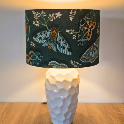 Lamp with a decorative green lampshade featuring moth illustrations showing the gold lining glowing when lit